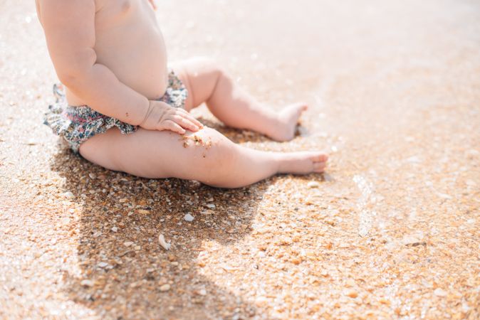 Crop view of anonymous cute baby sitting on beach
