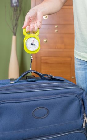 Woman checking luggage weight with a hand balance