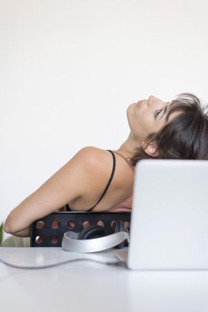 Tired woman leaning back at desk with laptop