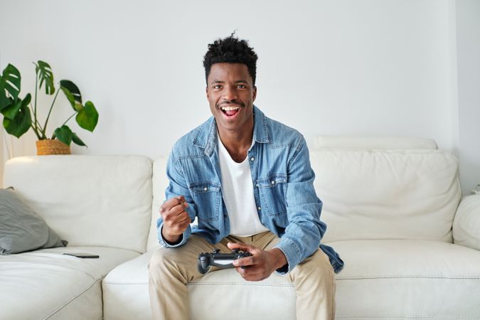 Excited Black man playing video game with joystick on couch