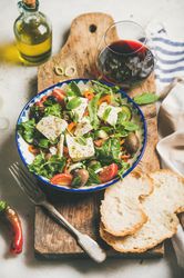 Greek salad with feta, tomatoes, and red wine on wooden board, vertical composition, selective focus