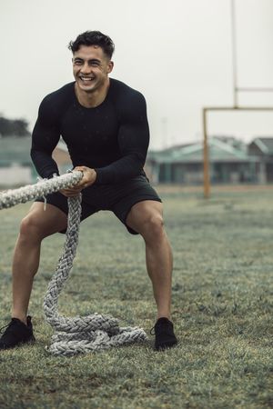 Happy athlete pulling rope for exercise outdoors in the rain