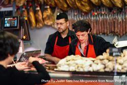 Man and woman in butcher shop serving a customer 0VlAr4
