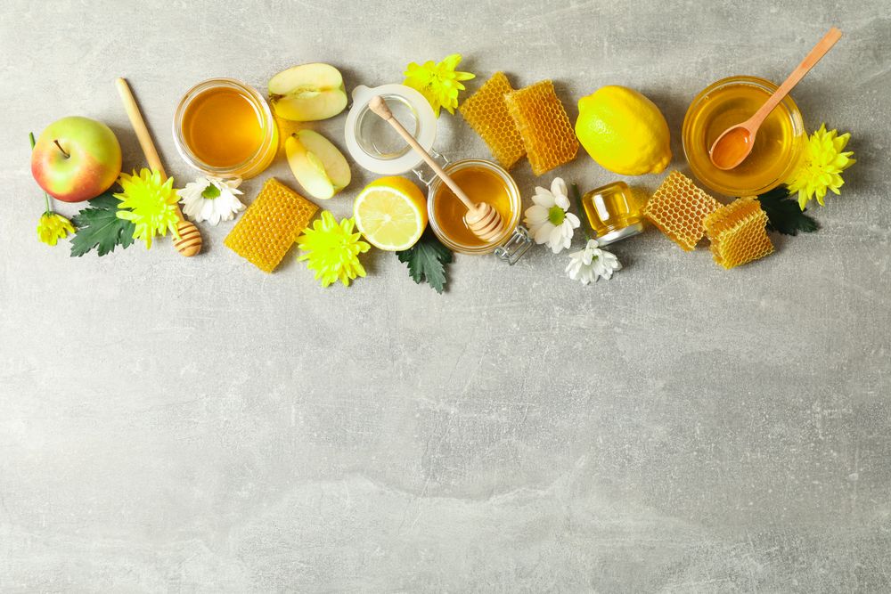 Flat lay with honey, flowers and fruits on grey background, copy space