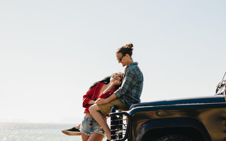 Happy young couple enjoying ocean views while parked with their car