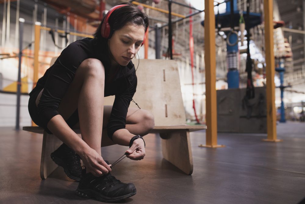 Smiling woman with headphones lacing shoe in gym