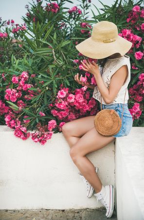 Woman sitting on white wall with pink oleander tree