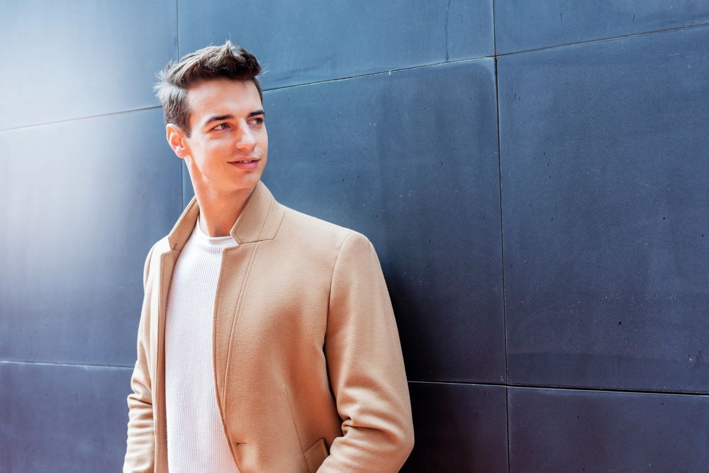 Young man wearing winter coat looking around against dark wall