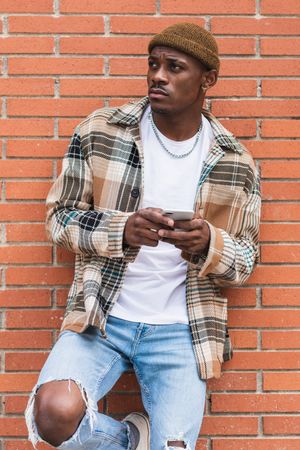 Black man using smartphone near brick wall
