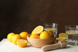 Bowl with lemons, juicer and lemonade on wooden table
