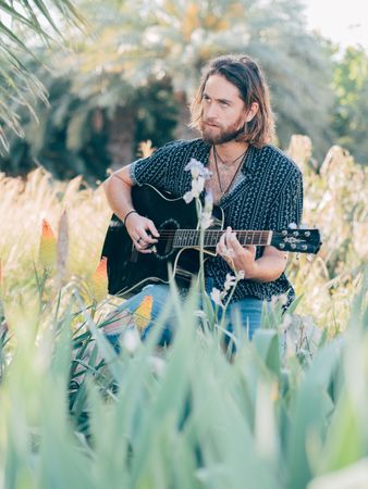 Hipster man in meadow with guitar