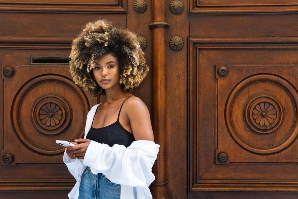 Serious Black woman browsing smartphone near old wooden door