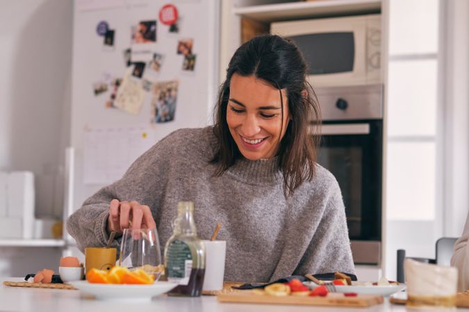 Cheerful woman at table with delicious breakfast in kitchen