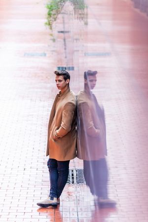 Man relaxing while leaning on reflective wall outside in autumn coat