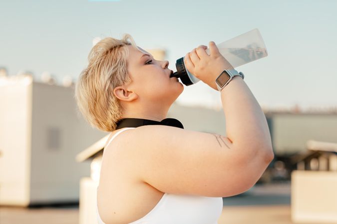 Blonde woman in exercise gear drinking from a water bottle outside