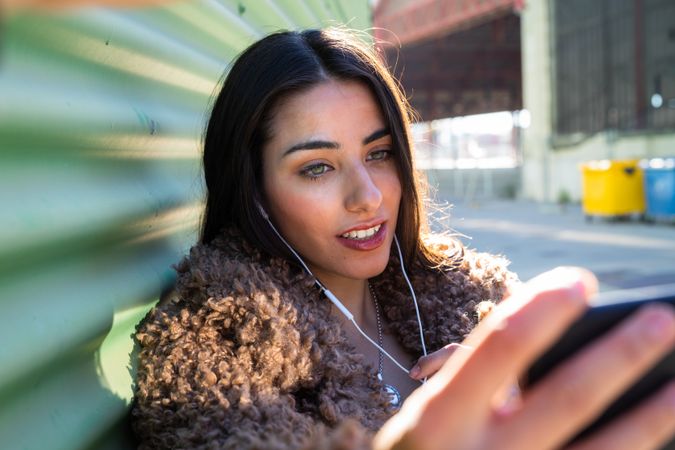 Trendy woman with smartphone near wall