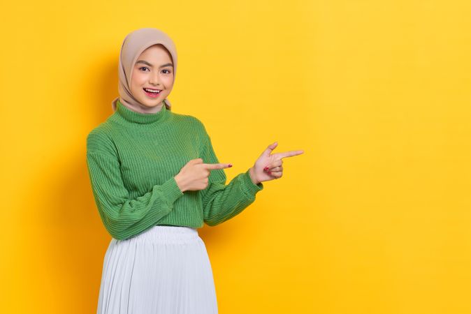 Woman in headscarf pointing at yellow copy space