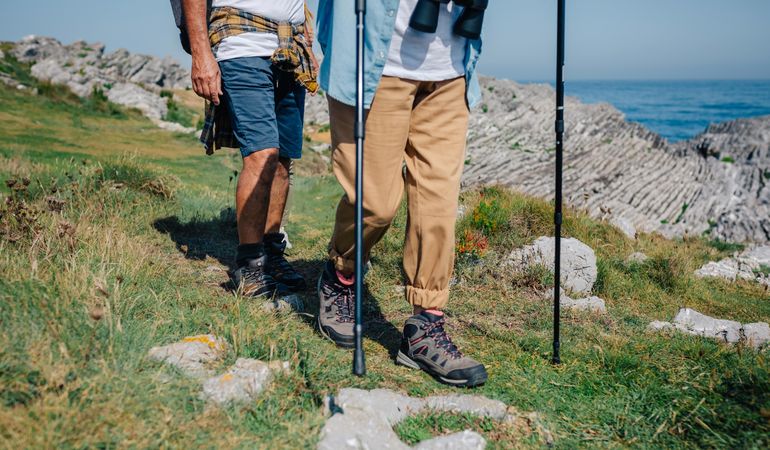 Legs of two hikers with poles on hill by ocean