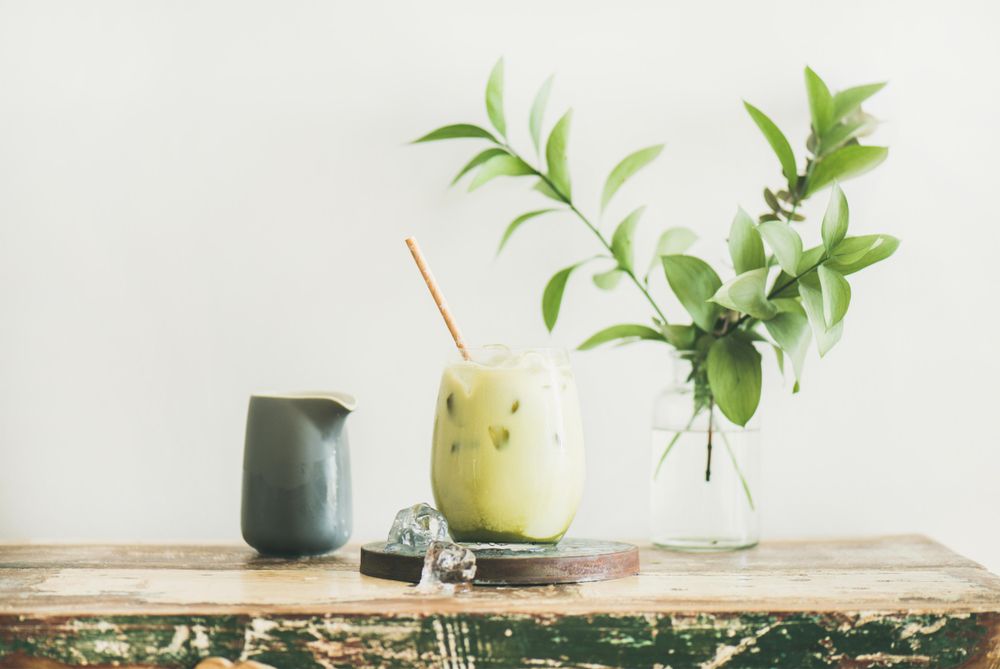 Iced matcha drink with creamer on side, with eco friendly straw and leaves, horizontal composition