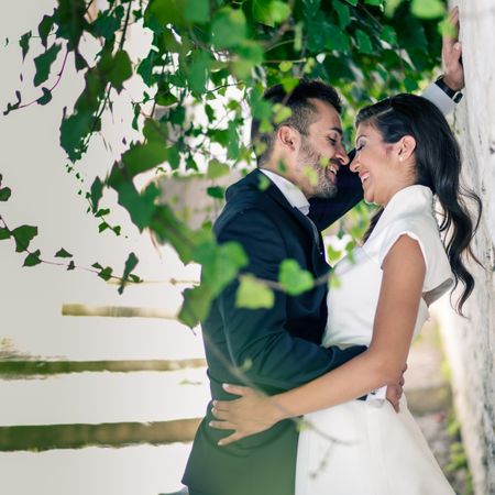 Happy newlywed couple facing each other under bright green branches
