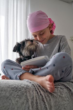 Boy in pink scarf with dog and writing in notebook