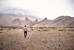 Unrecognizable male traveler walking on rocky terrain near hills