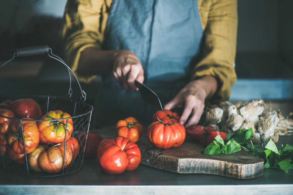 Woman in yellow chopping large tomatoes on wooden board