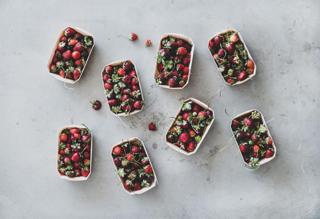 Strawberries in eco-friendly plastic-free boxes, scattered on concrete background