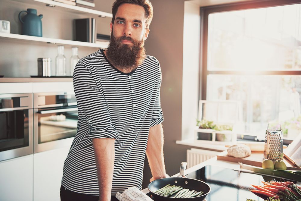 Man in bright kitchen cooking asparagus in pan