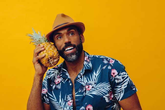 Happy male holding a pineapple to his cheek in yellow studio