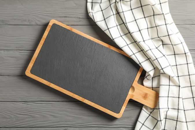 Kitchen towel with cutting board on wooden background, top view