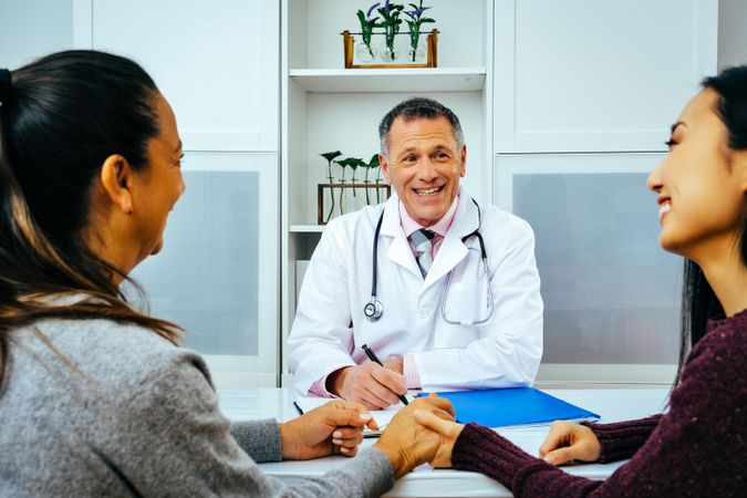 Happy doctor sharing news with two patients in medical office