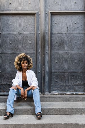 Stylish Black woman sitting on concrete steps near gates
