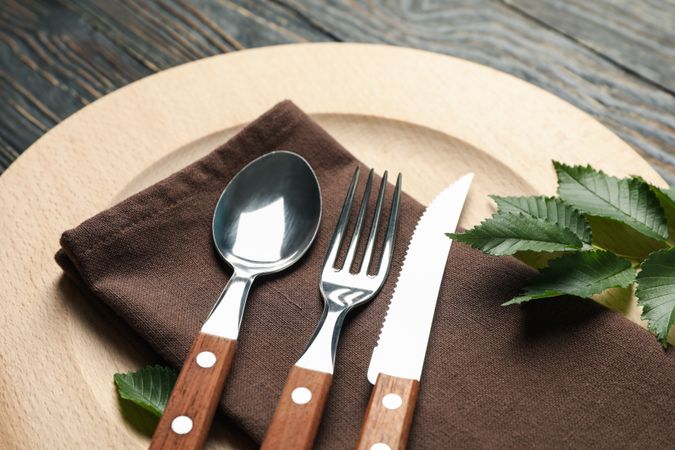 Table setting with wooden plate and cutlery on wooden background