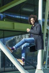 Portrait of cheerful Black man in jacket with warm beverage balancing between poles outside