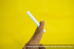 Side view of hand holding cigarette against yellow wall 4mWd2d