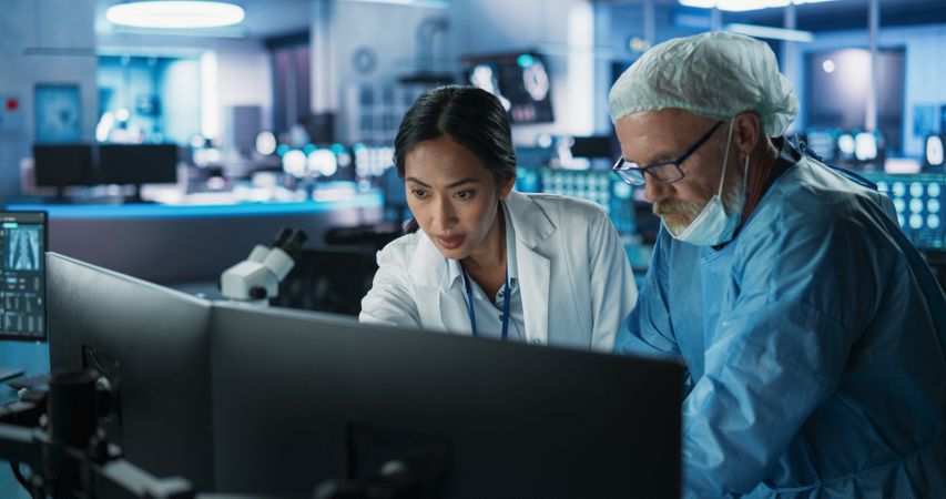 Medical Hospital Research Lab Meeting: Female Asian Neuroscientist Talking To Male Neurosurgeon About CT Brain Scans On Desktop Computer.