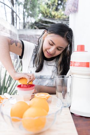 A young Hispanic woman is squeezing an orange to make orange and carrot juice outdoors