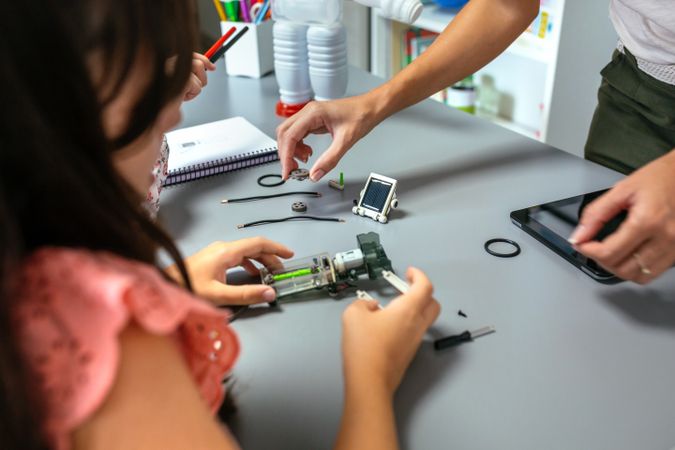 Female teacher helping girl students to assemble pieces of machine in a robotics class