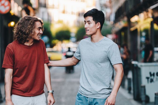 Cool multiracial male friends chatting while walking on street