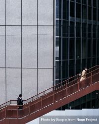 Two people climbing the an outdoor metal stairs near a high-rise building 428Qe0