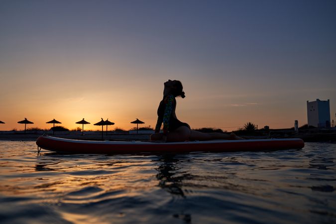 Fit female athlete taking Ardha Kapotasana pose on SUP board