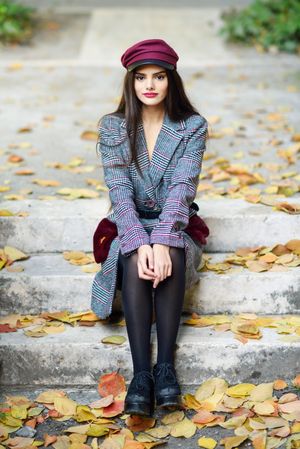 Female in warm winter clothes sitting on park steps with scattered fall leaves