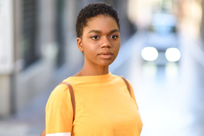 Portrait of female in yellow t-shirt standing on street with car in background