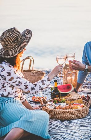 Couple toasting with wine glasses over summer picnic by the ocean