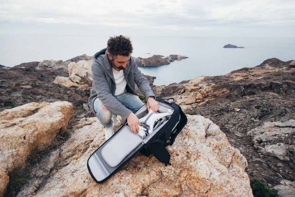 Man with backpack with drone equipment on a cliff