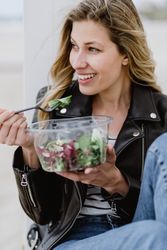 Content woman eating salad from plastic bowl sitting on wooden terrace