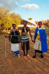 Two older women and on young woman hold hands outside at Zulu villagee