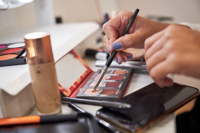 Crop woman taking colorful eyeshadow with brush