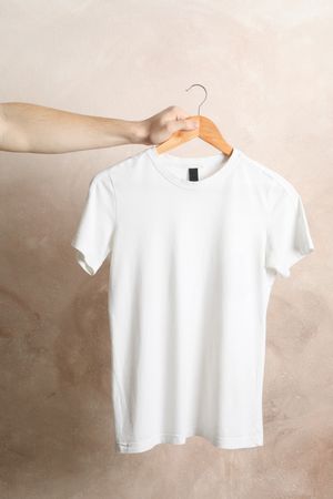 Man holds a hanger with blank t-shirt on brown background, space for text
